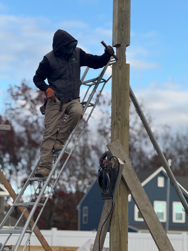 Worker climbing ladder hammering post